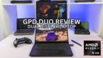 Dette billede viser en bærbar computer med to skærme med titlen &quot;GPD DUO REVIEW&quot;. Den bærbare computer har to skærme, den ene oven på den anden, hvor den øverste skærm viser en scene fra en film eller et tv-show, mens den nederste skærm viser et racerspil. Den bærbare computer har et tastatur i bunden, og der ligger en spilcontroller og en pen på bordet ved siden af. I baggrunden ses en hylde med andre bærbare computere og tekniske gadgets. AMD Ryzen 9 HX-processorens logo vises i nederste højre hjørne af billedet.