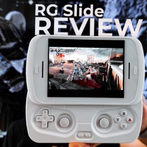 A first-person perspective image showing a pair of hands holding a white RG Slide handheld gaming console, centered in the frame. The console's screen displays an action-packed video game with multiple characters. In the background, a large monitor or screen shows a blurred image of a video game character, adding depth to the scene. Prominently overlaid in white text at the top are the words "RG Slide REVIEW". A black and white "DROIX" logo is visible in the bottom left corner.