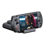 A black GPD WIN 5 handheld console is shown docked into its matching black chargingdata dock angled forward against a white background The consoles screen displays a close up image of a female character with pink hair and cybernetic enhancements The devices controls and the docks four LED indicators are clearly visible